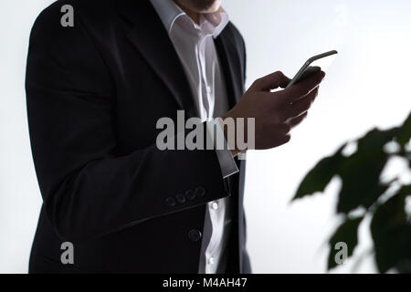 Mobile security, phisning and online crime. Businessman or man in a suit holding a smartphone in dark shadow. Financial fraud with smart device. Stock Photo