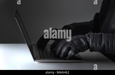 Cyber security threat, attack and online crime concept. Hacker writing with laptop computer wearing leather gloves. Stock Photo