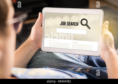 Man trying to find work with online job search engine on tablet. Jobseeker at home holding smart device. Motivated and happy applicant. Stock Photo