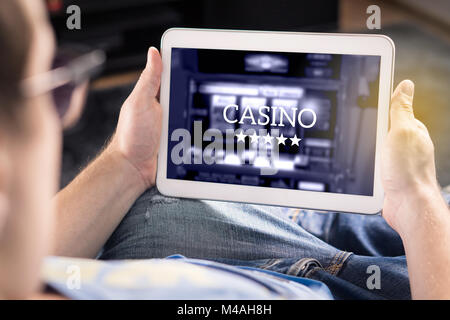 Man playing in an online casino with tablet. Modern gambling application. Slot machine app. Person holding smart mobile device in hand at home. Stock Photo