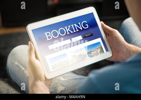 Booking app or website on tablet screen. Man searching hotel and flights for holiday and vacation with travel application. Person holding smart device Stock Photo