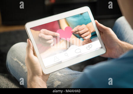 Online dating concept. Imaginary application or website. Finding love from internet using app. Man using and holding tablet and smart device at home. Stock Photo