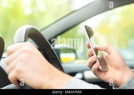 Man using smartphone while driving. Driver texting and sending sms and using mobile phone in car. Writing and typing message with cellphone in vehicle Stock Photo