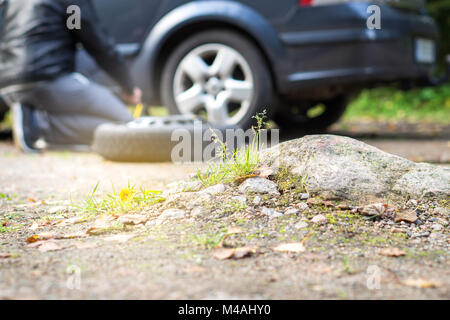 Broken and flat car tyre. Man changing new spare wheel after vehicle hit rock on countryside sand road. Driver fixing problem. Stock Photo