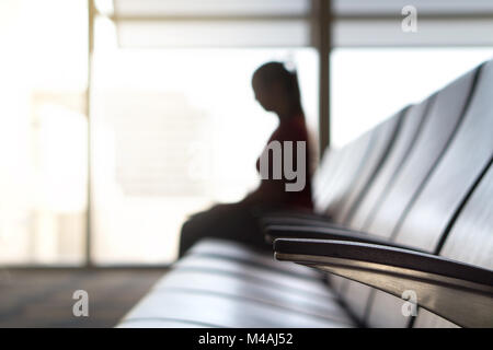Person sitting in waiting room at gate before boarding and flight. Silhouette woman in departure lounge at airport. Travel, holiday and transportation Stock Photo