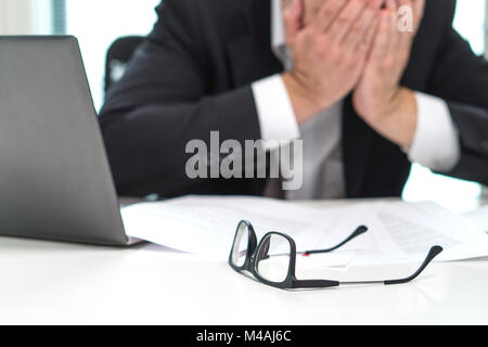 Stressed business man covering face with hands in office. Working over time or too much. Problem with failing business or confusion with crisis. Stock Photo