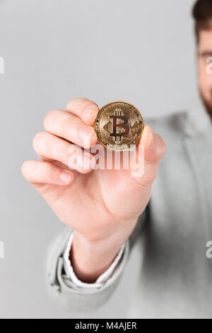 Close up of male hand showing golden bitcoin isolated over gray background Stock Photo