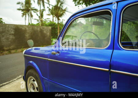 Side view on retro blue car in tropical city. Palms are on background. Stock Photo