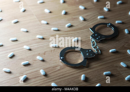 Drug addiction, medical abuse and narcotics hook and dependence concept. Handcuffs surrounded by many pills. Tablet overdose. Withdrawal symptoms Stock Photo