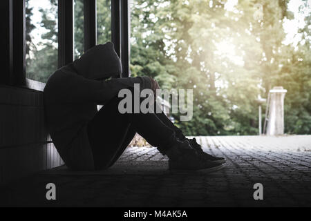 Depression, social isolation, loneliness, mental health and discrimination concept. Sad, lonely, depressed and unhappy man. Hooded person sitting. Stock Photo
