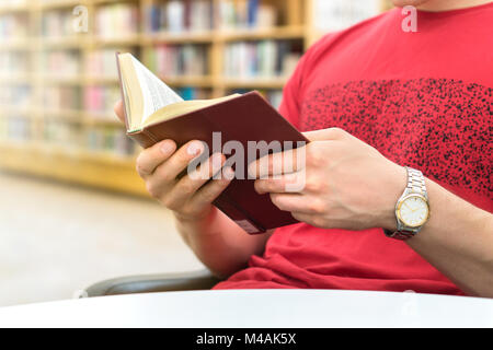 Young athletic man or student reading a book in public or school library in college or university. Education, studying and literature service concept. Stock Photo