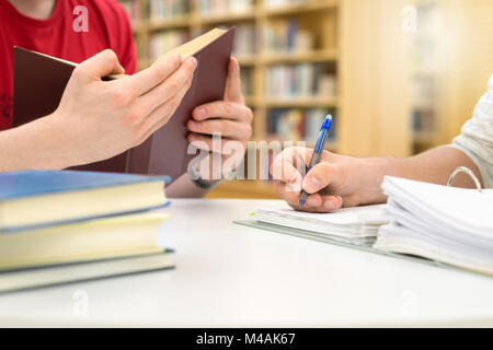 Two students studying, reading and writing in library. Friends working together on a school project, assignment or homework. Teamwork, cooperating. Stock Photo