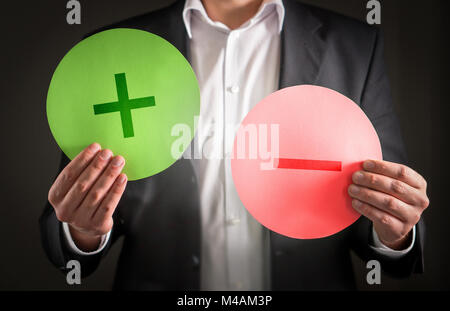 Pros and cons concept. Business man with cardboard plus and minus symbol signs. Stock Photo
