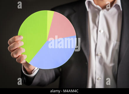 Business man holding a pie chart made from cardboard paper. Visual demonstration of finance statistics and market and sales situation. Stock Photo