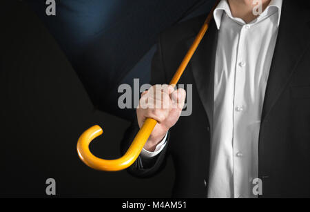 Business man holding umbrella with wooden handle on his shoulder with dark background. Sad unemployment, failure, bankruptcy, over work, burn out and  Stock Photo