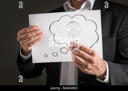 New idea, innovation and brainstorming concept. Business man in a suit holding light bulb and a paper with thinking speech bubble balloon and thought  Stock Photo