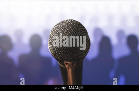 Close up of microphone in front of a silhouette audience and crowd of people. Public speaking and giving speech. Stage fright or training to talk. Stock Photo