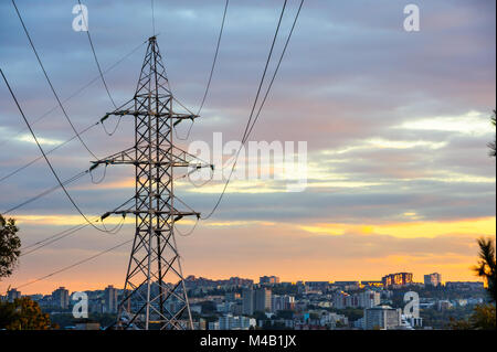 Electricity pylons and power lines silhouettes at a cloudy sunset. Stock Photo