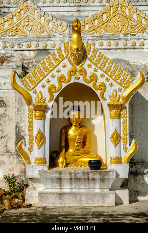 A golden Buddha statue is sitting in a little shrine in one of many golden Pagodas on top of Sagaing Hill Stock Photo