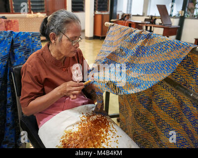 Craftswoman applying hot wax-resist dyeing on batik with a canting (spouted tool). Batik Winotosastro shop, Yogyakarta, Java, Indonesia. Stock Photo