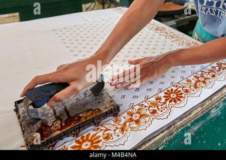 Batik maker block prints on a cloth with a Cap (copper stamp). Batik Winotosastro shop, Yogyakarta, Java, Indonesia. Stock Photo
