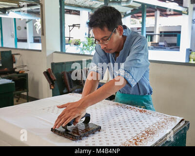 Batik maker prints hot wax on a cloth with a copper stamp. Batik Winotosastro shop, Yogyakarta, Java, Indonesia. Stock Photo