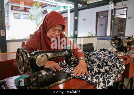 A woman sews a batik shirt using a vintage sewing machine. Batik Winotosastro shop, Yogyakarta, Java, Indonesia. Stock Photo