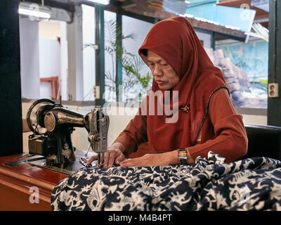A woman sews a batik shirt using vintage sewing machine. Batik Winotosastro shop, Yogyakarta, Java, Indonesia. Stock Photo