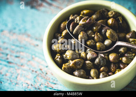 Capers in the bowl on the light blue background Stock Photo