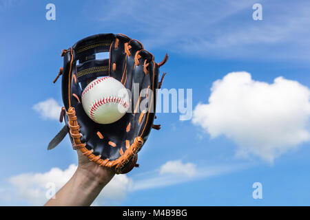 Hand holding baseball in glove with blue sky Stock Photo