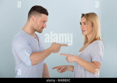 Angry Couple Pointing At Each Other Against Colored Background Stock Photo