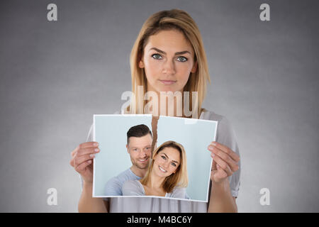 Portrait Of A Young Woman Holding Torn Photo Against Grey Background Stock Photo
