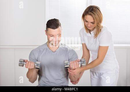 Young Smiling Female Physiotherapist Helping A Man To Exercise With Dumbbells Stock Photo