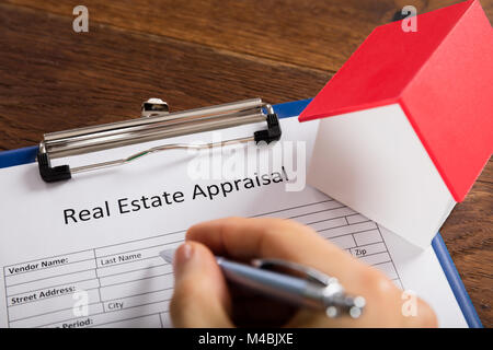 Close-up Of Person Hand Filling Real Estate Appraisal Form With House Model At Desk Stock Photo