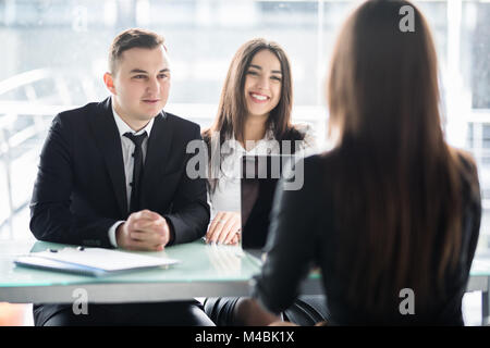 Happy couple meeting with a broker in her office leaning over the desk Stock Photo