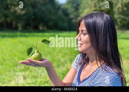 Colombian woman looking at pear on hand outside Stock Photo