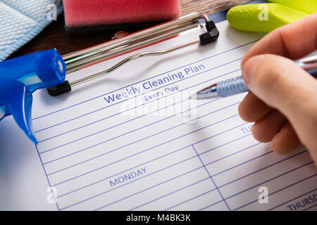 Close-up Of Person Hand Filling Weekly Cleaning Plan Form With Pen Stock Photo