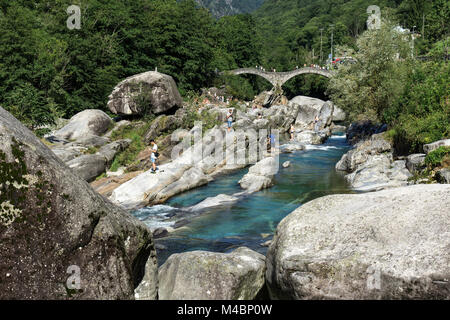 Rock formations,bathing people at Verzasca near Lavertezzo,in the back the Roman bridge Ponte dei Salti,Verzascatal Stock Photo