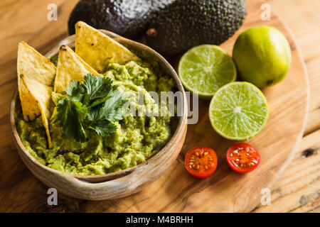 Tortilla chips in a bowl of guacamole dip with avocado limes and cherry tomato ingredients Stock Photo