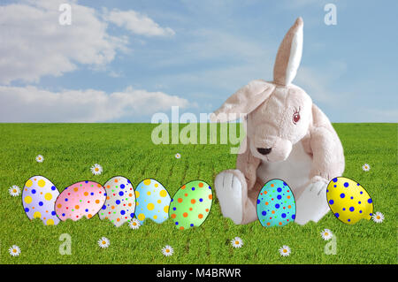 photographic montage stuffed rabbit with colored eggs in a meadow Stock Photo