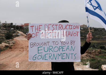 Nativ Ha'avot, Israel. 15th Feb, 2018. An activist from the right wing Zionist organization Im Tirtzu holds a sign reading “the destruction of Netiv Ha’avot, brought to you by European governments” in a counter protest to leftists from Peace Now movement who arrived to Nativ Ha'avot following Israeli government attempts to postpone the removal of some of the houses in the Jewish outpost despite the Supreme Court ruling. Credit: Eddie Gerald/Alamy Live News
