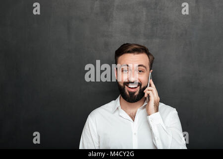 Attractive man talking on smartphone having pleasant conversation looking on camera over graphite background copy space Stock Photo