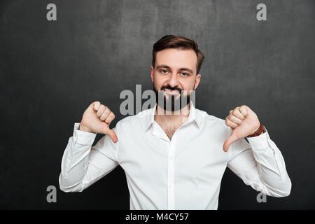 Picture of disappointed guy 30s gesturing on camera with thumbs down over dark gray background Stock Photo