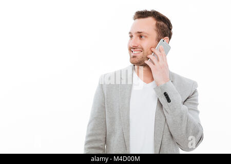 Portrait of businesslike guy in jacket having pleasant mobile conversation using cellphone and looking aside over white background Stock Photo
