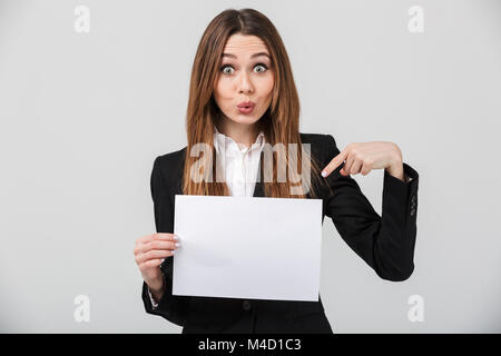 Funny pretty lady dressed in suit grimacing and pointing at blank white sheet isolated over grey wall Stock Photo