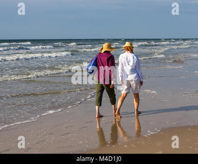 Two American senior citizen women walk together on a beach in the early morning. Stock Photo