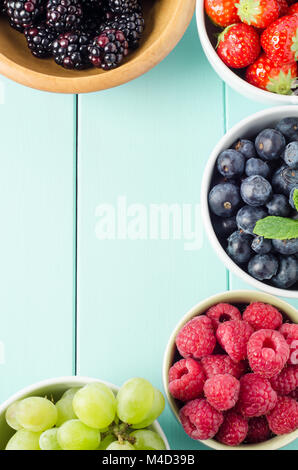 Overhead shot of five fruit varieties in separate bowls bordering frame edge of aqua blue wood planked table. Stock Photo