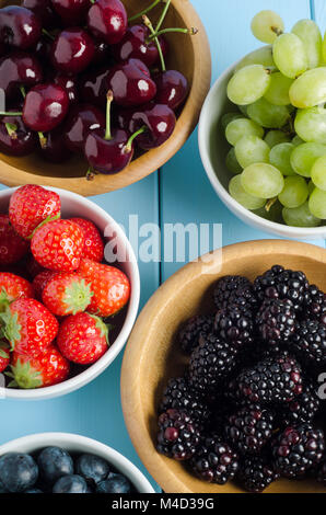 Overhead shot of five different fruit choices in separated bowlls on blue wood plank table. Stock Photo