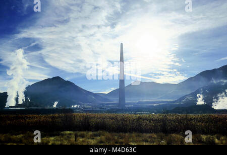 A smokestack spewing white vapor into the air on a bright blue sky. Stock Photo