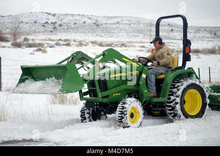 A farmer plowing snow with a john deere tractor. Stock Photo